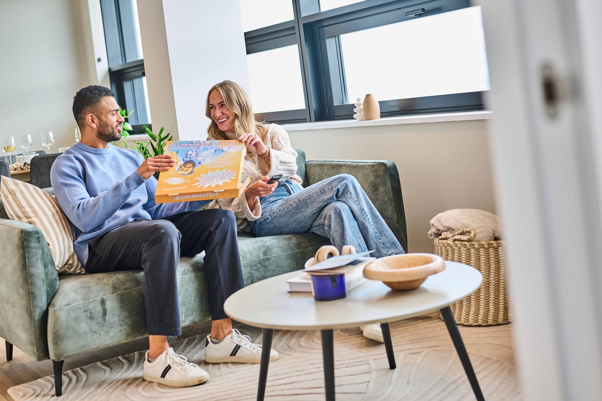 Male and female tenants enjoying pizza on a sofa in a high-end rental apartment at The Octagon